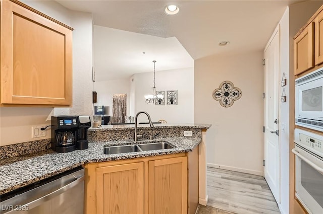 kitchen with a sink, light brown cabinets, a peninsula, and white appliances