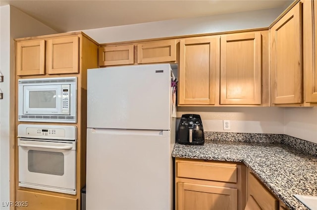 kitchen with light brown cabinets, dark stone countertops, and white appliances