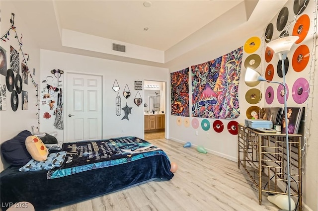 bedroom featuring a tray ceiling, baseboards, visible vents, and wood finished floors