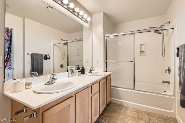 bathroom with visible vents, a sink, shower / bath combination with glass door, and double vanity