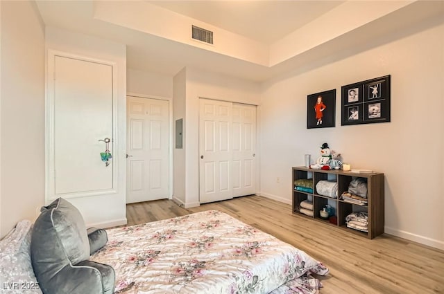 bedroom featuring a raised ceiling, wood finished floors, baseboards, and visible vents