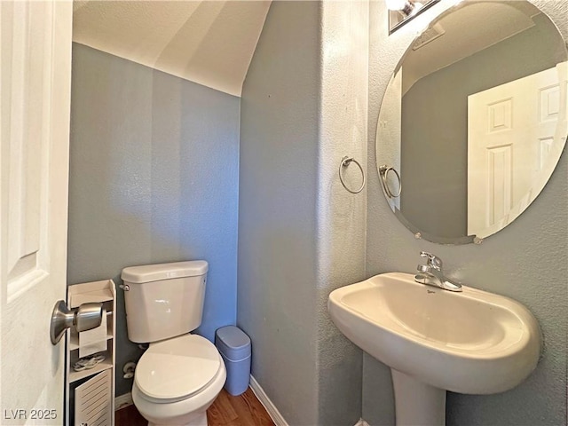 bathroom featuring a textured wall, toilet, a sink, wood finished floors, and baseboards