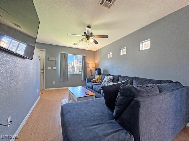 living room with a textured wall, visible vents, baseboards, a ceiling fan, and light wood finished floors