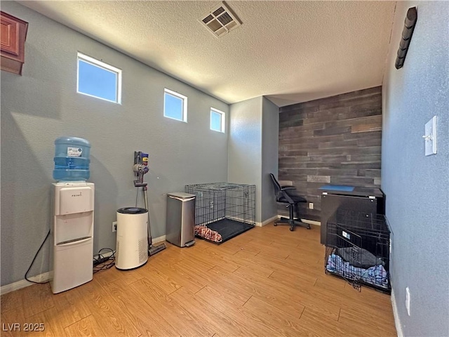 miscellaneous room with light wood finished floors, wooden walls, visible vents, and a textured ceiling