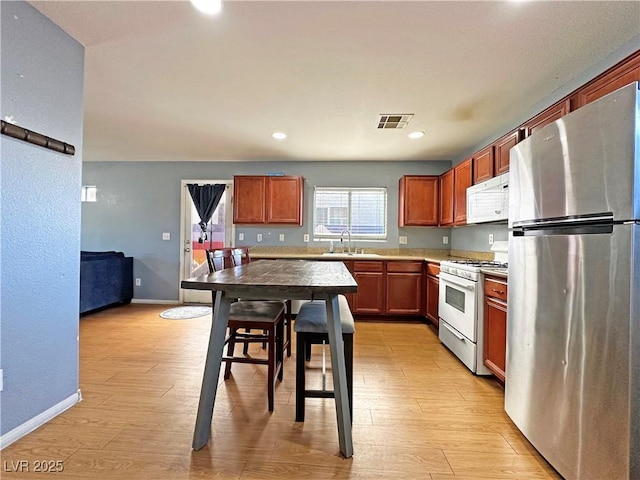 kitchen featuring light wood-style floors, white appliances, visible vents, and a sink