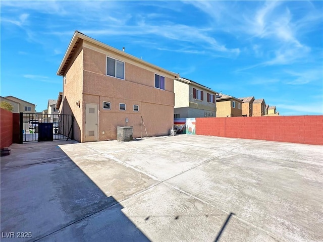 rear view of property with a gate, stucco siding, fence, and central AC unit