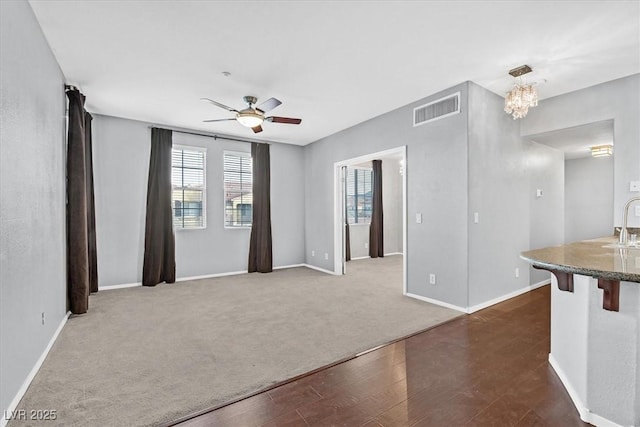 unfurnished living room featuring baseboards, visible vents, dark wood-style flooring, and ceiling fan with notable chandelier