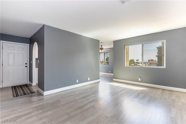 unfurnished living room featuring arched walkways, baseboards, and wood finished floors