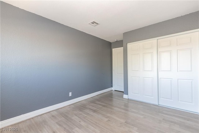 unfurnished bedroom featuring a closet, visible vents, light wood-style flooring, and baseboards