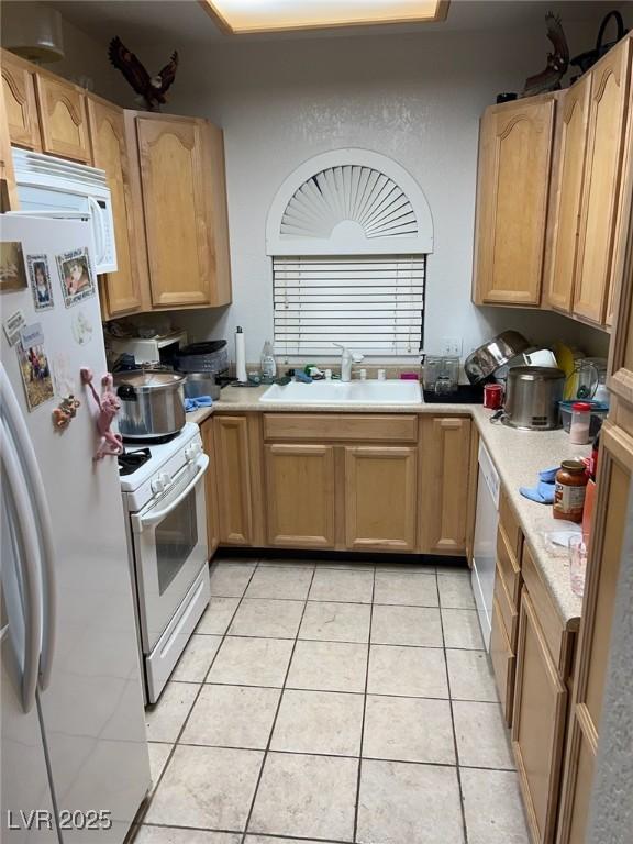 kitchen with light tile patterned floors, white appliances, a sink, light countertops, and light brown cabinetry