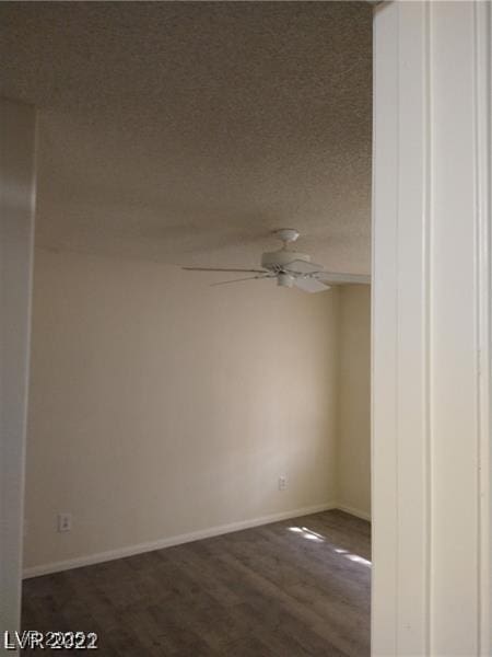 empty room with ceiling fan, a textured ceiling, baseboards, and dark wood-style flooring