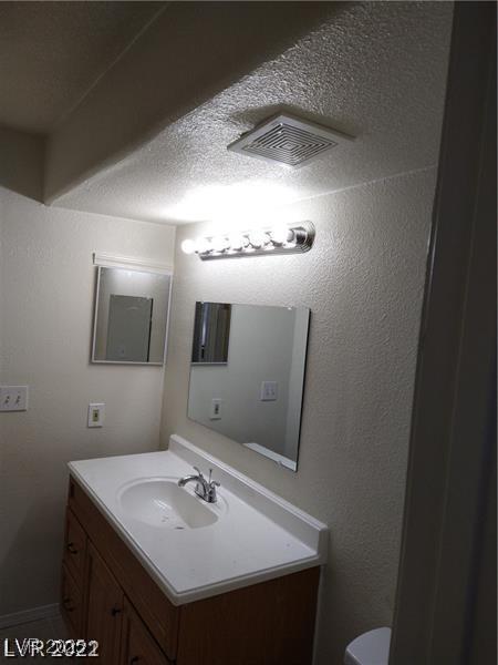 half bath featuring a textured wall, visible vents, and vanity