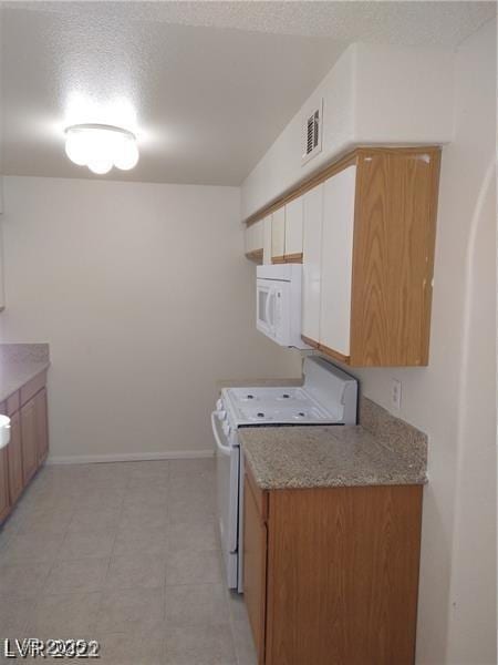 kitchen featuring a textured ceiling, white appliances, visible vents, and baseboards