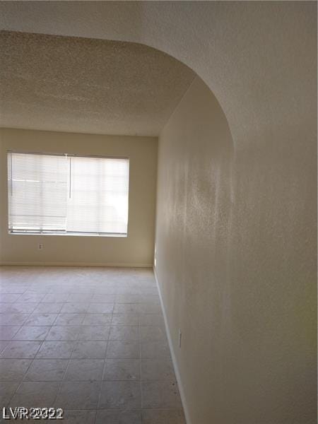 empty room with baseboards, arched walkways, and a textured ceiling