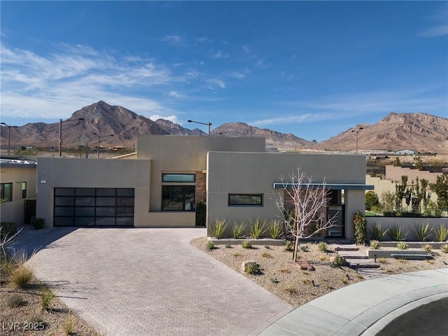 view of front facade featuring decorative driveway, a mountain view, an attached garage, and stucco siding