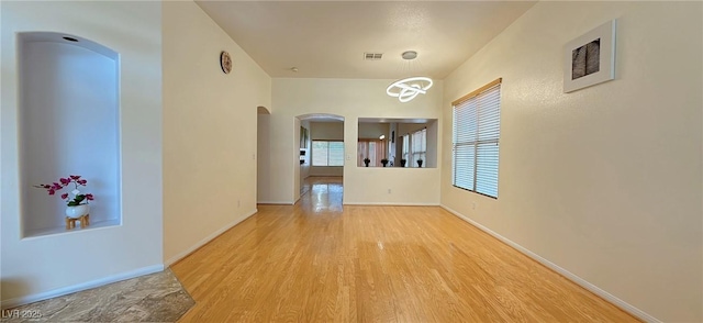 empty room featuring arched walkways, wood finished floors, visible vents, and baseboards