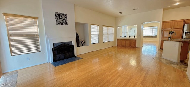 unfurnished living room featuring a fireplace with flush hearth, arched walkways, a sink, and light wood-style flooring