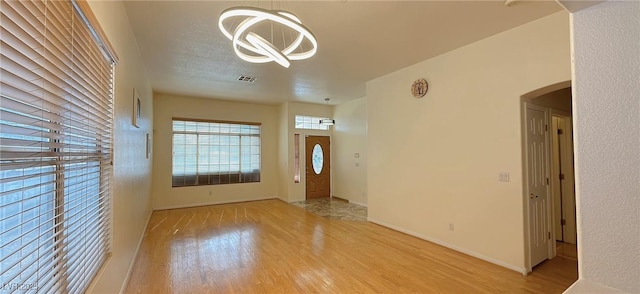 entryway with visible vents, light wood-style flooring, a textured ceiling, a chandelier, and baseboards