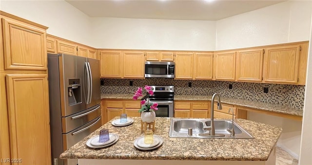 kitchen featuring an island with sink, a sink, light stone countertops, stainless steel appliances, and backsplash