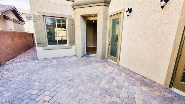 property entrance featuring stucco siding, fence, and a patio