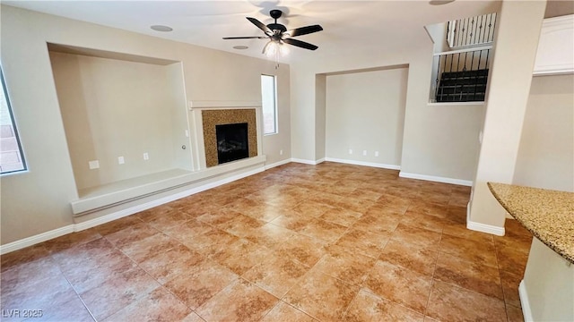 unfurnished living room with a glass covered fireplace, a ceiling fan, and baseboards