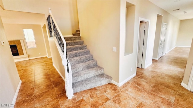 stairway featuring visible vents, baseboards, and a glass covered fireplace