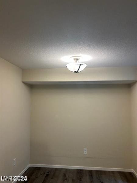 spare room with a textured ceiling, dark wood-type flooring, and baseboards