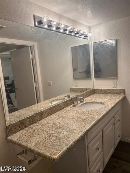 bathroom with a textured ceiling, a textured wall, wood finished floors, and vanity