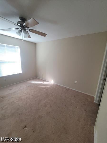 carpeted spare room featuring ceiling fan and baseboards