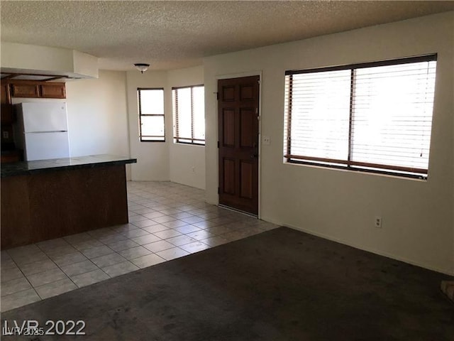 kitchen featuring light tile patterned floors, light colored carpet, a textured ceiling, and freestanding refrigerator