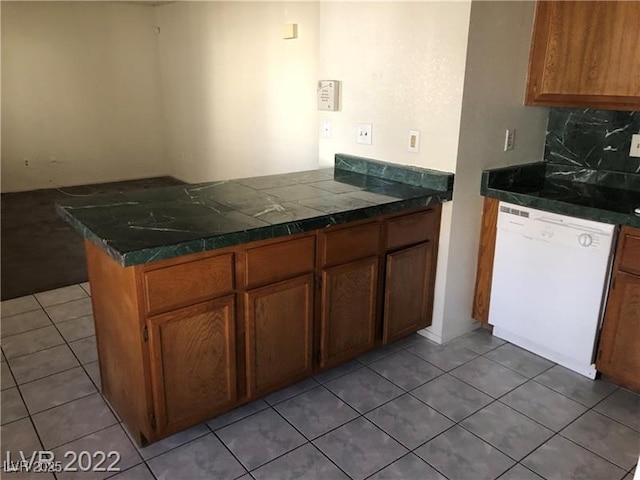 kitchen featuring brown cabinetry, decorative backsplash, a peninsula, tile patterned flooring, and white dishwasher