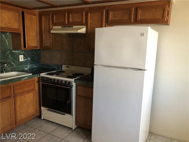 kitchen with light tile patterned floors, decorative backsplash, a sink, white appliances, and under cabinet range hood