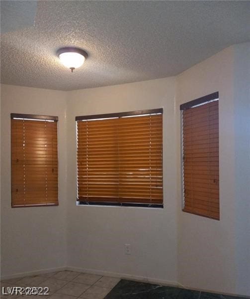 empty room featuring tile patterned flooring, a textured ceiling, and baseboards