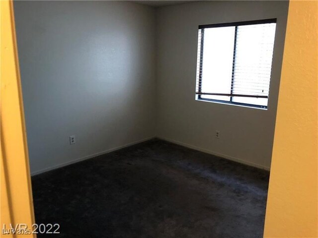 spare room featuring baseboards and dark colored carpet