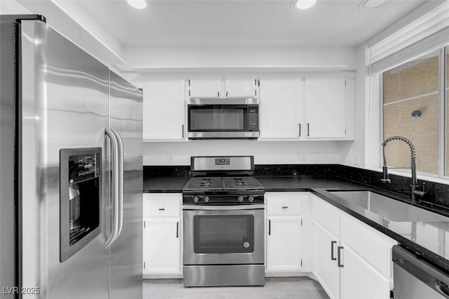 kitchen with appliances with stainless steel finishes, dark stone counters, white cabinetry, and a sink