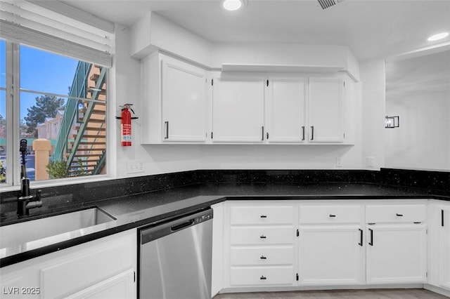 kitchen with dark countertops, white cabinets, a sink, and stainless steel dishwasher