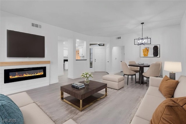 living area featuring a glass covered fireplace, visible vents, and wood finished floors