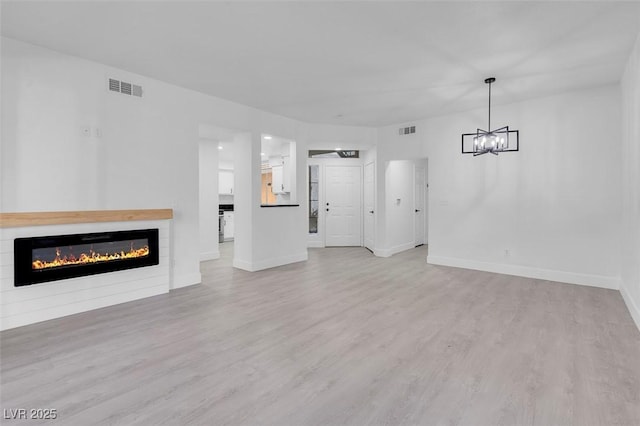 unfurnished living room featuring a glass covered fireplace, visible vents, and wood finished floors