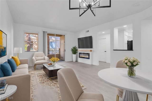 living area with a chandelier, light wood-style flooring, a glass covered fireplace, and visible vents