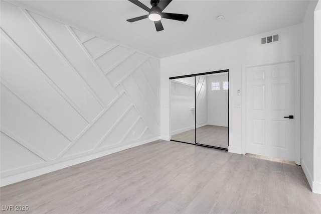 unfurnished bedroom with a closet, visible vents, a decorative wall, light wood-style flooring, and ceiling fan