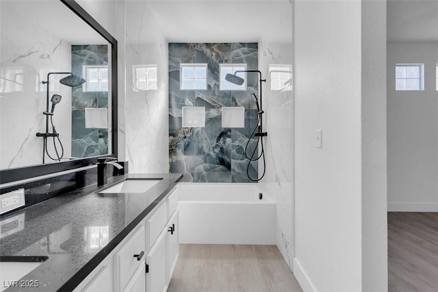 bathroom with a combined bath / shower with marble appearance, baseboards, wood finished floors, and vanity