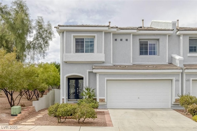 view of front of house with a garage, a tile roof, driveway, french doors, and stucco siding