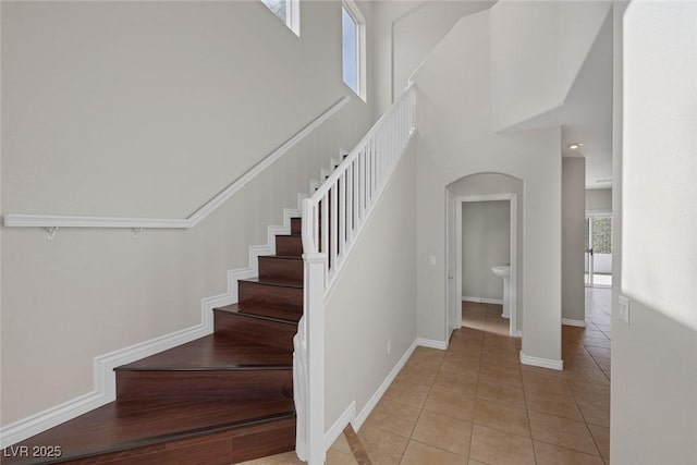 stairs with arched walkways, a towering ceiling, baseboards, and tile patterned floors