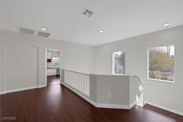 unfurnished room featuring baseboards, wood-type flooring, visible vents, and a healthy amount of sunlight