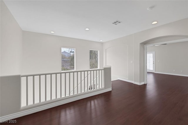 spare room featuring arched walkways, recessed lighting, wood finished floors, visible vents, and baseboards