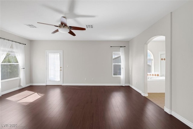 empty room featuring arched walkways, hardwood / wood-style flooring, and visible vents