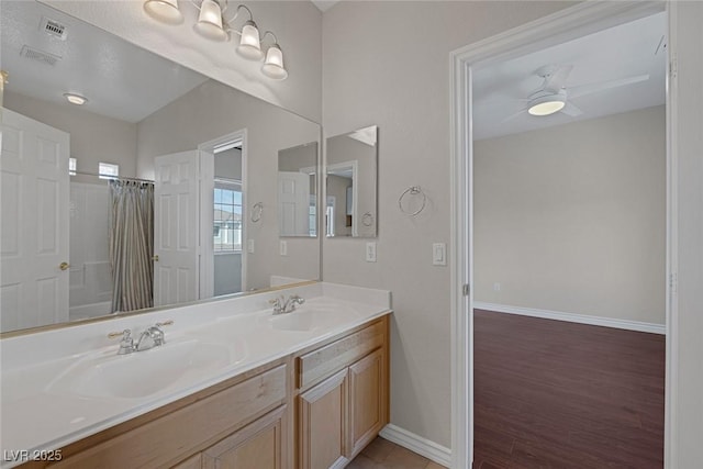 full bath featuring double vanity, baseboards, a ceiling fan, and a sink