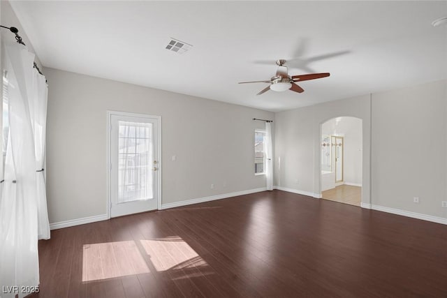 spare room featuring arched walkways, visible vents, a ceiling fan, wood finished floors, and baseboards