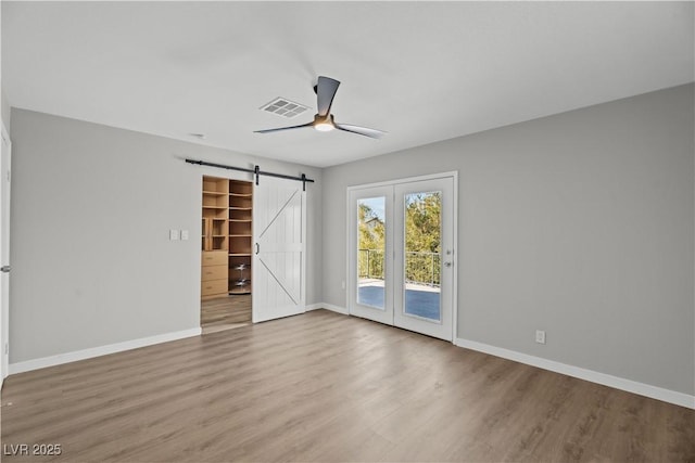 empty room featuring ceiling fan, a barn door, wood finished floors, visible vents, and baseboards