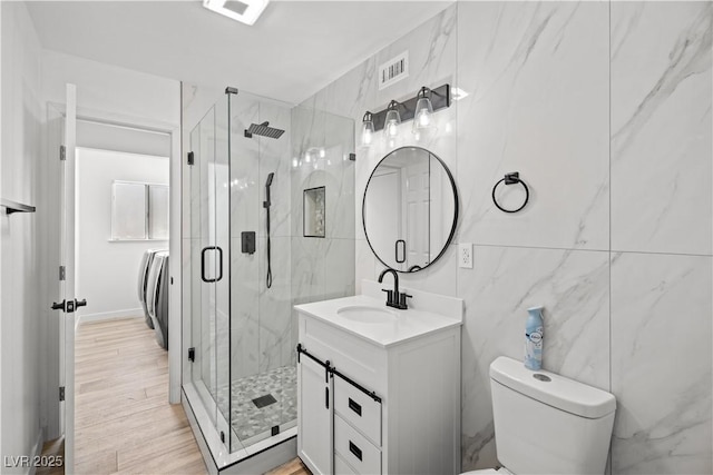 bathroom featuring visible vents, vanity, a marble finish shower, and tile walls